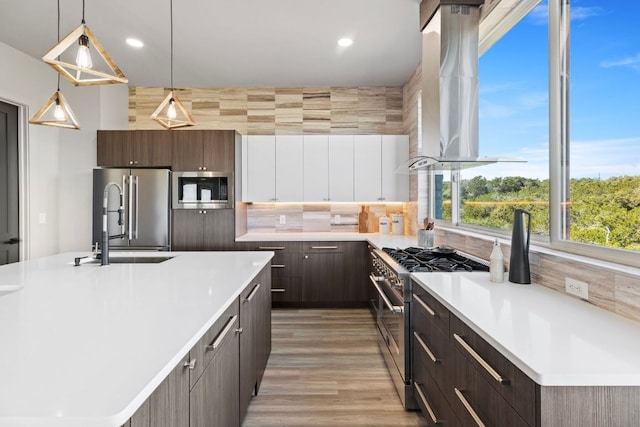 kitchen featuring light countertops, premium appliances, decorative backsplash, wall chimney exhaust hood, and a sink