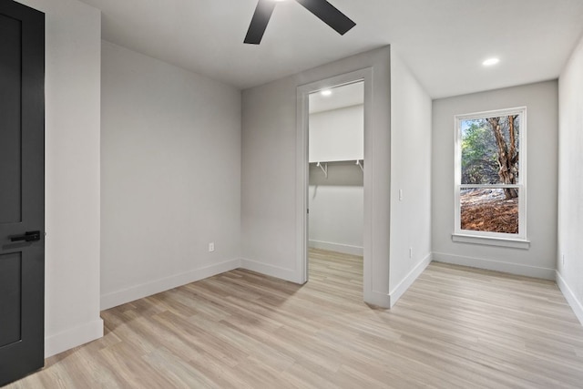 unfurnished bedroom with a ceiling fan, a spacious closet, baseboards, and light wood-type flooring