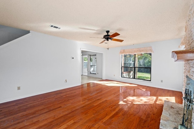 unfurnished living room featuring a wealth of natural light, visible vents, a stone fireplace, and wood finished floors