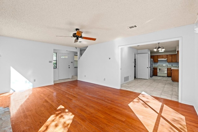 unfurnished living room with ceiling fan with notable chandelier, light wood-style floors, and visible vents