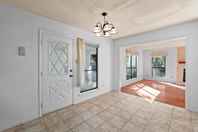 entrance foyer featuring light tile patterned floors, a textured ceiling, a stone fireplace, and an inviting chandelier