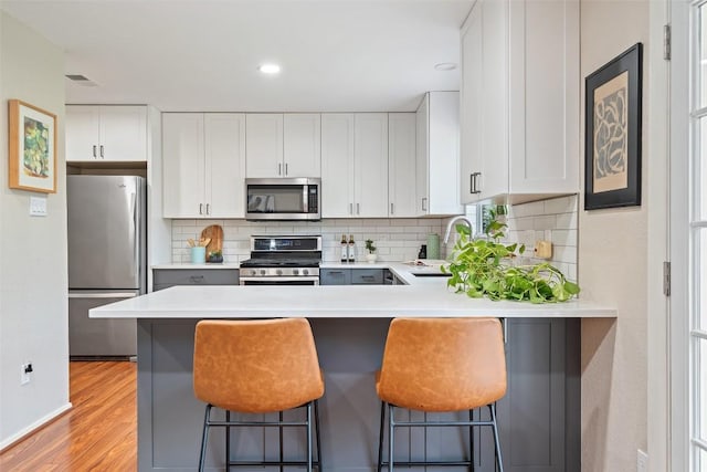 kitchen with light countertops, decorative backsplash, appliances with stainless steel finishes, light wood-style floors, and a sink