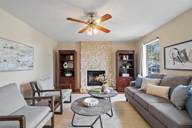 living area featuring a stone fireplace, light wood-type flooring, and ceiling fan