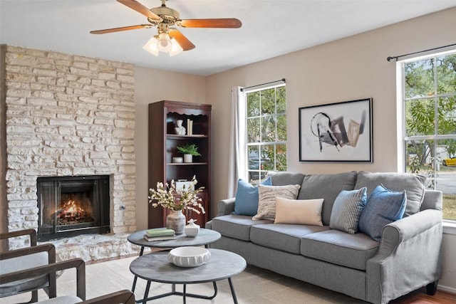 living area featuring ceiling fan, a stone fireplace, and wood finished floors