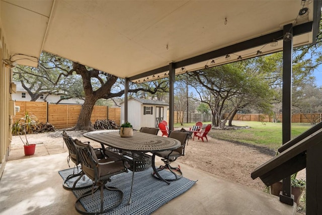 view of patio / terrace with an outbuilding, outdoor dining area, a fenced backyard, and a shed