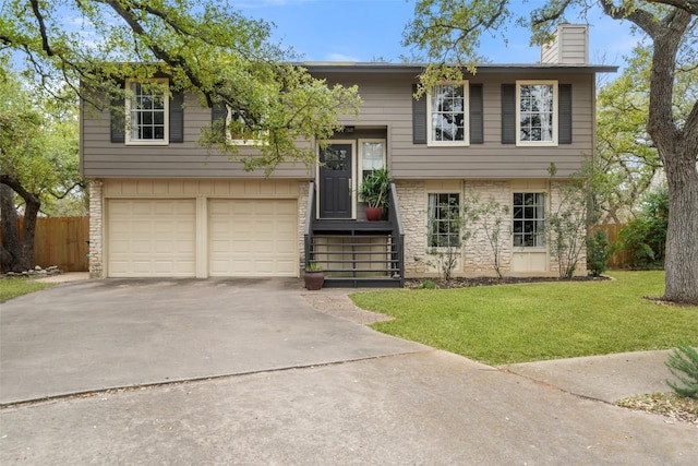 raised ranch featuring a front yard, fence, a chimney, concrete driveway, and a garage