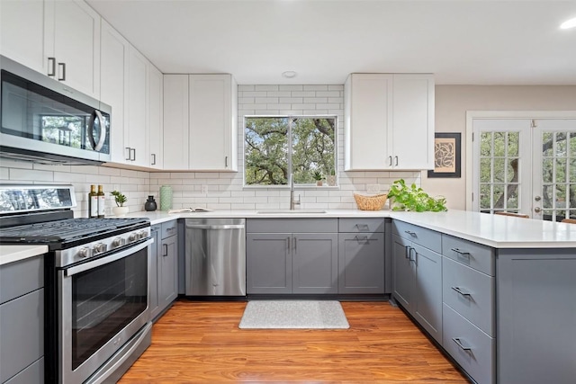 kitchen featuring appliances with stainless steel finishes, a peninsula, gray cabinetry, and a sink