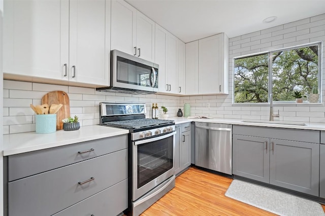 kitchen with a sink, gray cabinetry, appliances with stainless steel finishes, light wood-type flooring, and backsplash