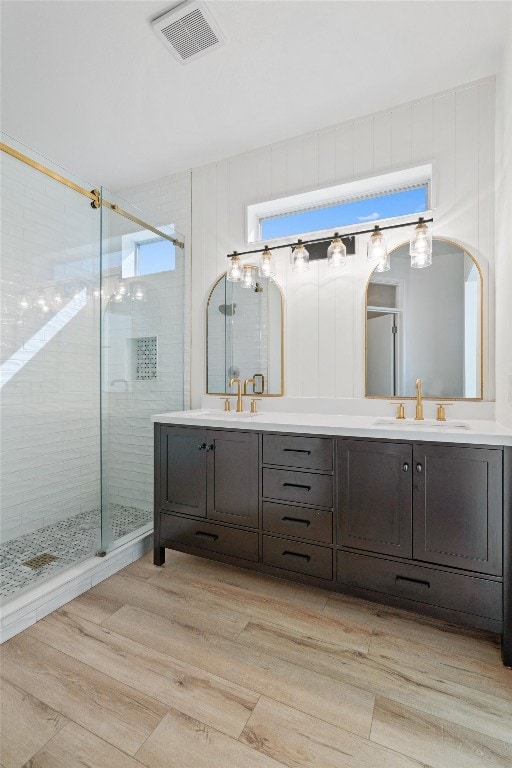 full bathroom with visible vents, a sink, wood finished floors, a shower stall, and double vanity