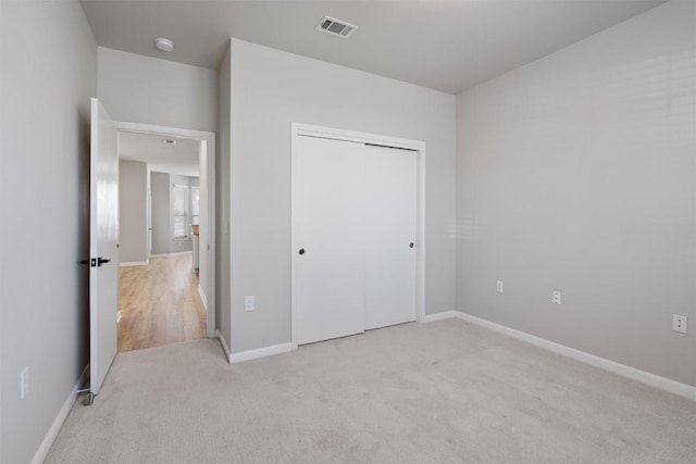 unfurnished bedroom with light carpet, visible vents, a closet, and baseboards