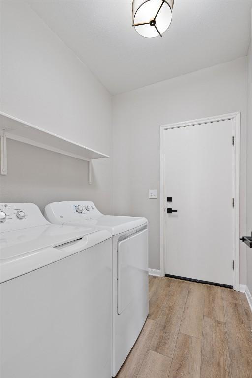 washroom with laundry area, separate washer and dryer, light wood-type flooring, and baseboards