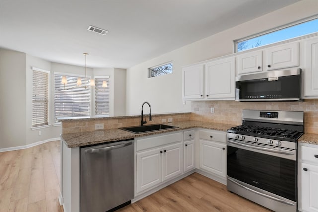 kitchen featuring visible vents, a peninsula, a sink, appliances with stainless steel finishes, and backsplash