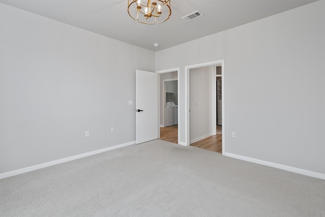 carpeted empty room with washer / dryer, visible vents, baseboards, and an inviting chandelier