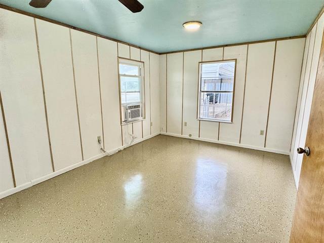 empty room with a decorative wall, cooling unit, speckled floor, and ceiling fan