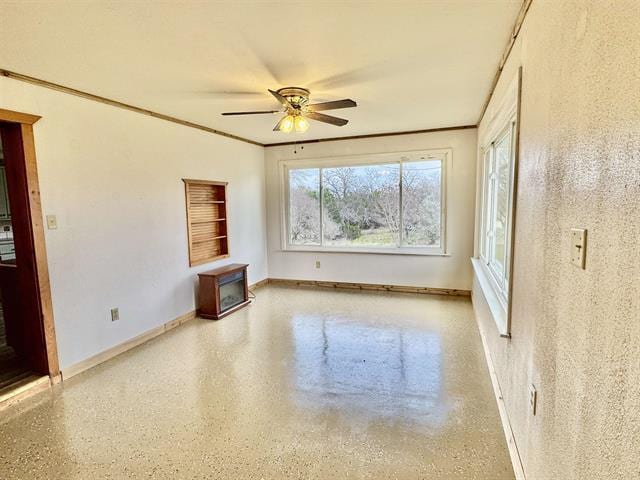 empty room with speckled floor, baseboards, a ceiling fan, and crown molding