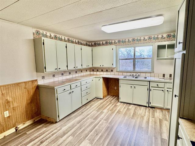 kitchen with a sink, light countertops, wainscoting, and light wood finished floors