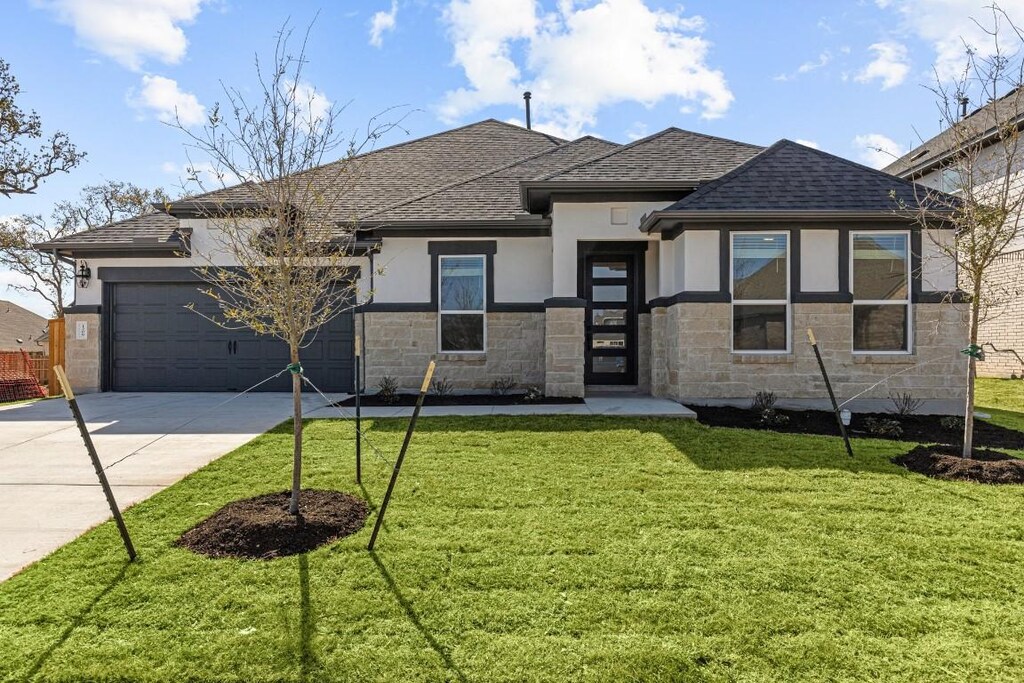 view of front of home featuring driveway, a front yard, stone siding, roof with shingles, and stucco siding