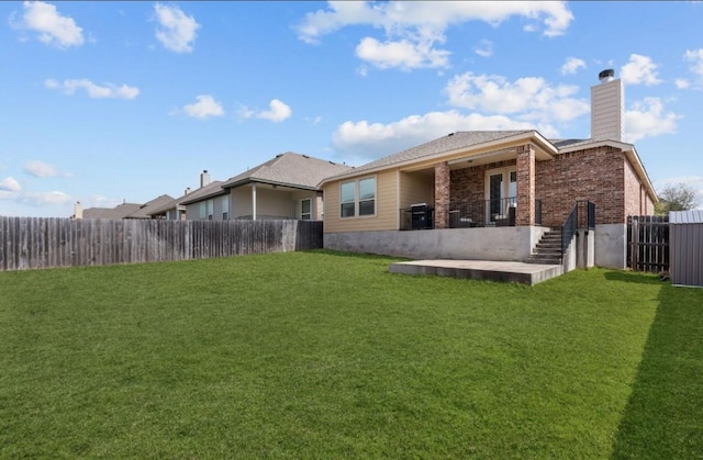 rear view of house featuring a patio, a fenced backyard, a yard, brick siding, and a chimney