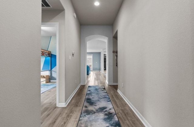 hall featuring visible vents, arched walkways, baseboards, and wood finished floors