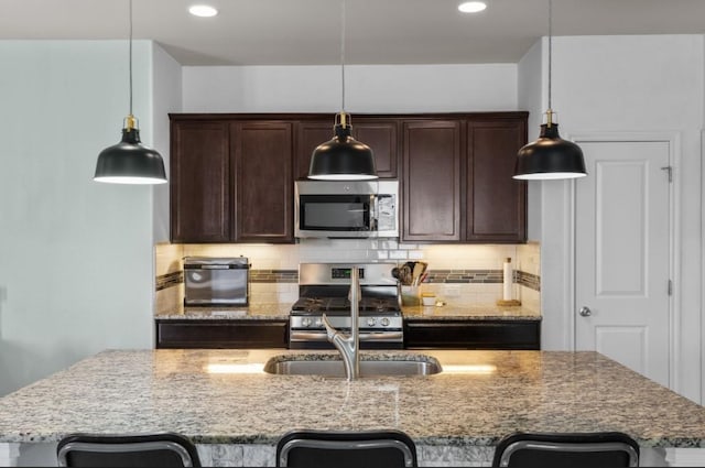 kitchen featuring an island with sink, a sink, dark brown cabinets, appliances with stainless steel finishes, and tasteful backsplash