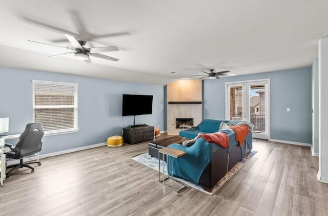 living room featuring a fireplace, wood finished floors, baseboards, and a ceiling fan