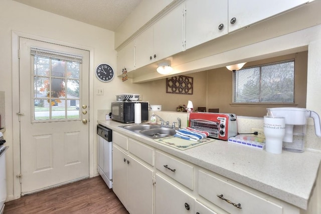 kitchen with black microwave, light countertops, dishwashing machine, white cabinetry, and a sink