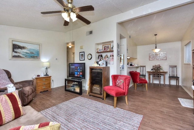 living room featuring lofted ceiling, wood finished floors, visible vents, and a textured ceiling