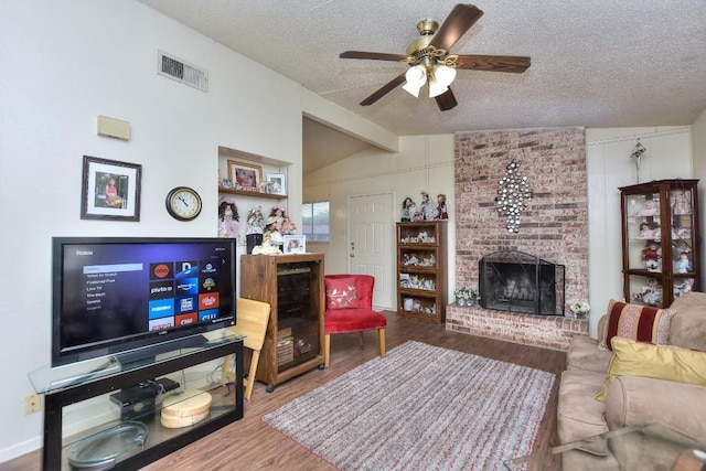 living area with visible vents, a brick fireplace, lofted ceiling with beams, wood finished floors, and a textured ceiling