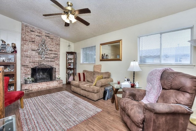 living room featuring a brick fireplace, lofted ceiling, wood finished floors, a textured ceiling, and a ceiling fan