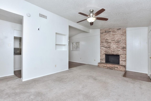 unfurnished living room featuring a ceiling fan, carpet, visible vents, a textured ceiling, and a brick fireplace