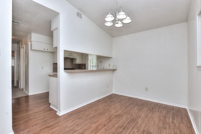 kitchen with a textured ceiling, a notable chandelier, wood finished floors, and vaulted ceiling