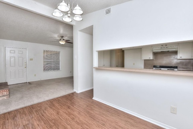 unfurnished living room with wood finished floors, baseboards, visible vents, a textured ceiling, and ceiling fan with notable chandelier