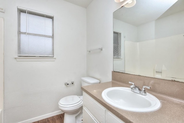 bathroom with vanity, toilet, wood finished floors, and baseboards