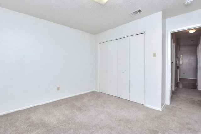 unfurnished bedroom featuring carpet flooring, visible vents, a closet, and a textured ceiling