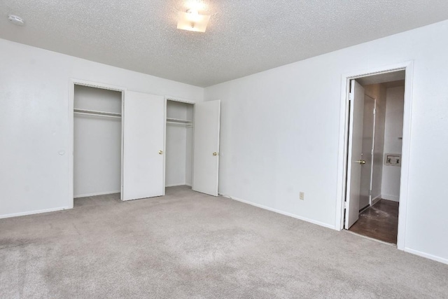 unfurnished bedroom featuring carpet flooring, baseboards, two closets, and a textured ceiling