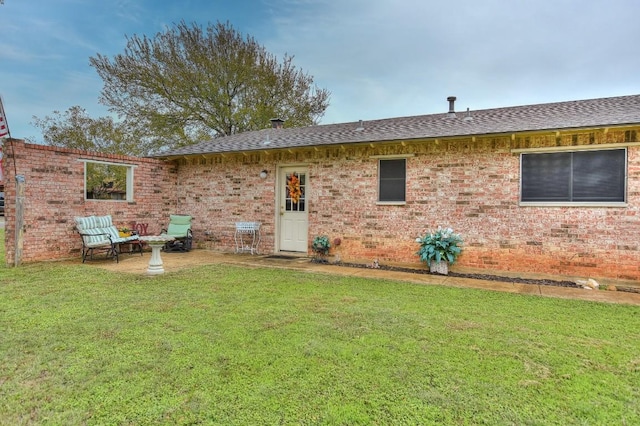 rear view of house featuring a patio, a lawn, roof with shingles, and brick siding