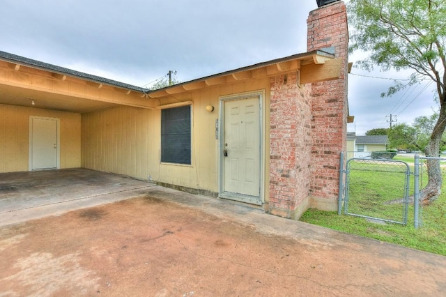 property entrance with a gate, fence, an attached carport, a chimney, and a patio area