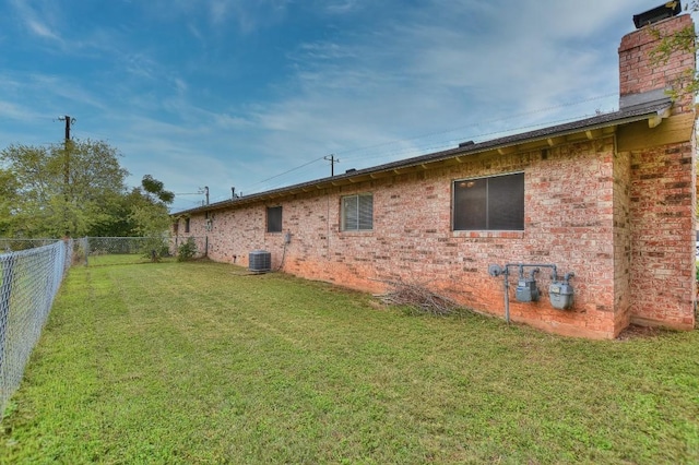 exterior space featuring central air condition unit, a lawn, a fenced backyard, brick siding, and a chimney