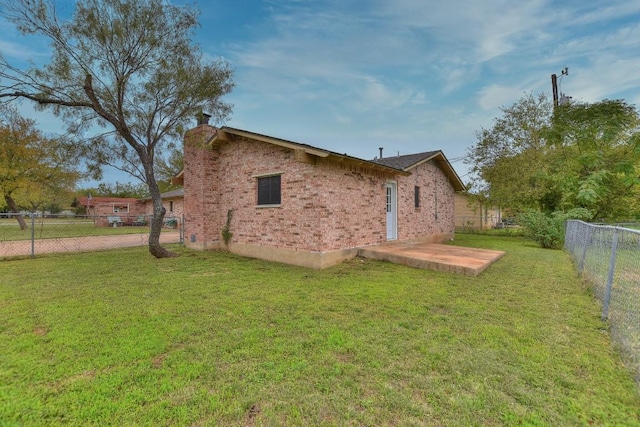 view of side of property featuring a patio, a fenced backyard, a chimney, a lawn, and brick siding