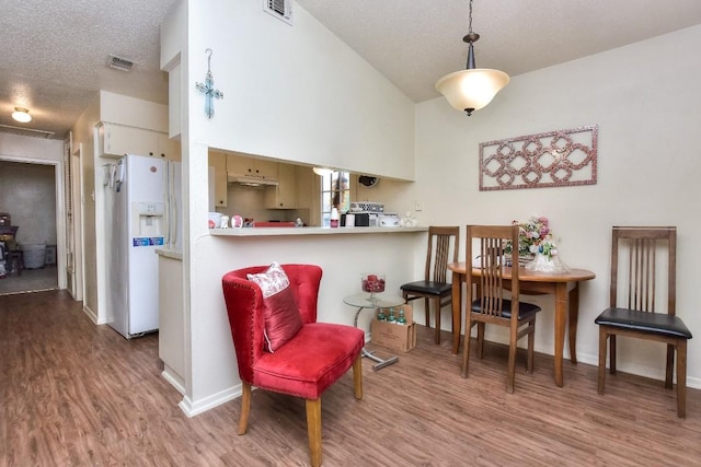 interior space with white refrigerator with ice dispenser, wood finished floors, visible vents, and a textured ceiling