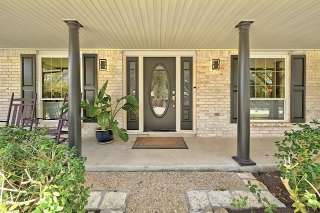 view of exterior entry featuring brick siding and covered porch