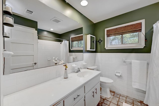 full bath with vanity, a wainscoted wall, visible vents, tile walls, and toilet