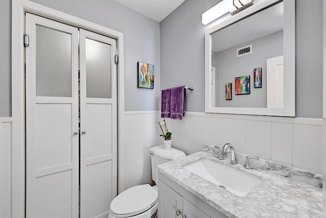 bathroom featuring visible vents, vanity, wainscoting, and toilet