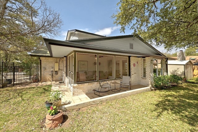 back of property featuring brick siding, fence, an outdoor structure, a sunroom, and a yard