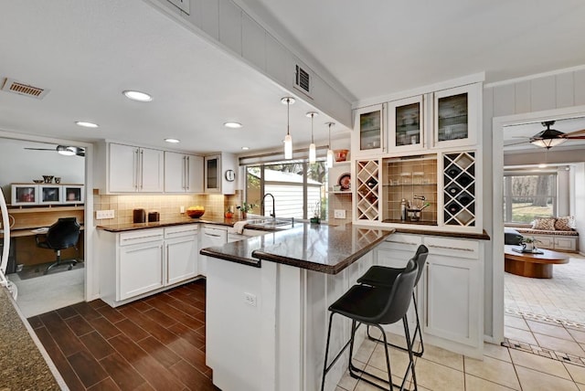 kitchen featuring glass insert cabinets, visible vents, a peninsula, and a kitchen bar