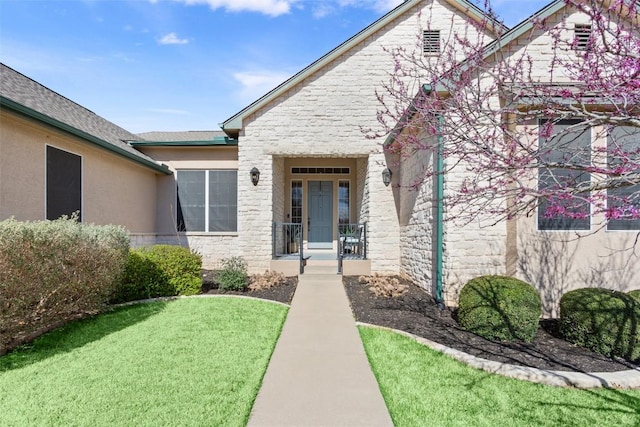 property entrance featuring stucco siding, stone siding, and a yard