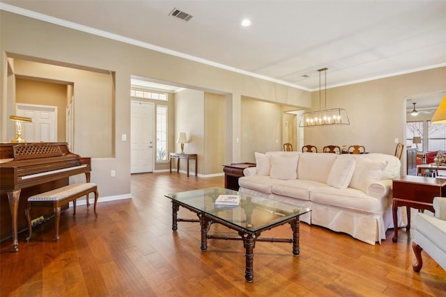 living area featuring visible vents, crown molding, baseboards, a chandelier, and wood finished floors