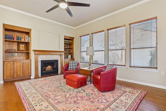 sitting room featuring ornamental molding, a ceiling fan, wood-type flooring, a fireplace, and baseboards