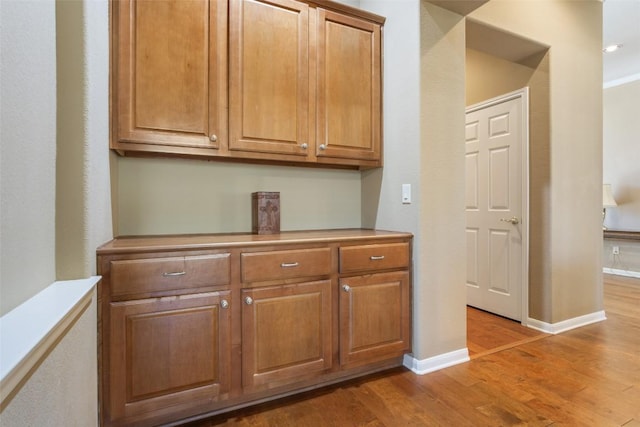 kitchen featuring brown cabinetry, light countertops, light wood-type flooring, and baseboards