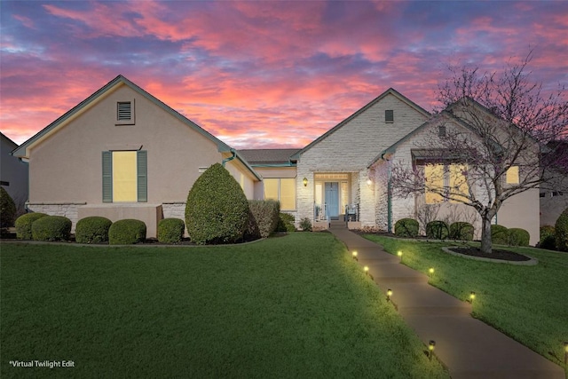 view of front of property featuring stone siding, stucco siding, and a yard